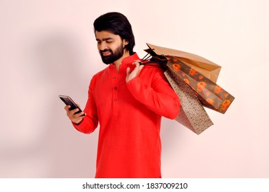 Young Indian Man Wearing Kurta With Shopping Bags & Using A Mobile Phone And Smiling While Doing Online Shopping 