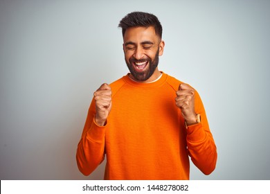 Young Indian Man Wearing Orange Sweater Over Isolated White Background Excited For Success With Arms Raised And Eyes Closed Celebrating Victory Smiling. Winner Concept.