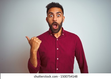 Young Indian Man Wearing Red Elegant Shirt Standing Over Isolated Grey Background Surprised Pointing With Hand Finger To The Side, Open Mouth Amazed Expression.