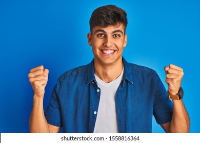 Young Indian Man Wearing Shirt Standing Over Isolated Blue Background Celebrating Surprised And Amazed For Success With Arms Raised And Open Eyes. Winner Concept.