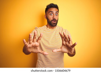 Young Indian Man Wearing T-shirt Standing Over Isolated Yellow Background Afraid And Terrified With Fear Expression Stop Gesture With Hands, Shouting In Shock. Panic Concept.