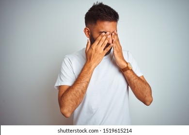 Young indian man wearing t-shirt standing over isolated white background rubbing eyes for fatigue and headache, sleepy and tired expression. Vision problem
