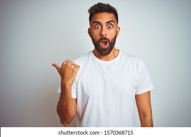 Young Indian Man Wearing T-shirt Standing Over Isolated White Background Surprised Pointing With Hand Finger To The Side, Open Mouth Amazed Expression.