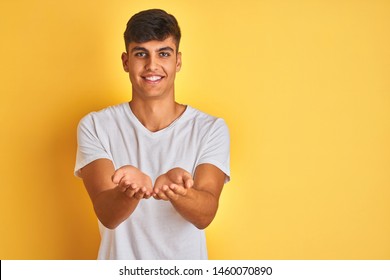 Young Indian Man Wearing White T-shirt Standing Over Isolated Yellow Background Smiling With Hands Palms Together Receiving Or Giving Gesture. Hold And Protection