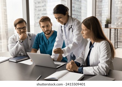 Young Indian medical team leader presenting job application on laptop to colleagues. Diverse doctors meeting at computer, talking on group video call, looking at screen, speaking, listening - Powered by Shutterstock