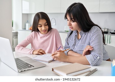 Young indian mother helping teen daughter remote studying at home explaining doing homework together. Parent mom teaching teenage school child distance learning online virtual class on computer.