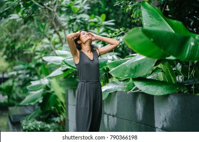 Young Indian professional lady enjoying a moment in the sun and brushing her hands through her long hair while standing. She is in a lush, green garden in the sunshine.  - Powered by Shutterstock