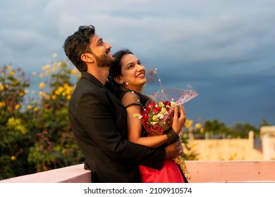 Young Indian romantic couple party attire celebrating anniversary, engagement, prewedding, wedding, festival, event, marriage, valentine day. Smiling, proposal, flower bouquet together, love, cuddle. - Powered by Shutterstock