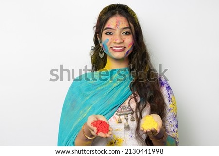Young indian smart girl with color powder in her hand and with face coloured with gulal for festival of colours Holi, a popular hindu festival celebrated across india, isolated over white background
