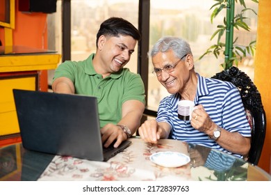 Young Indian Son And Old Father Using Laptop Together. Younger Generation Teaching Senior People How To Use Computer. Asian Family Using Internet Or Web Surfing At Home.