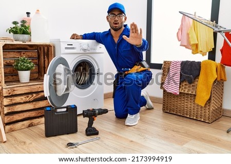 Young indian technician working on washing machine doing stop gesture with hands palms, angry and frustration expression 
