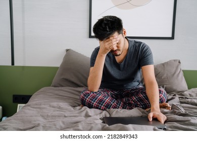 Young Indian Tired Man Closing Eyes With His Hand Holding Closed Laptop Sitting On Bed At Home