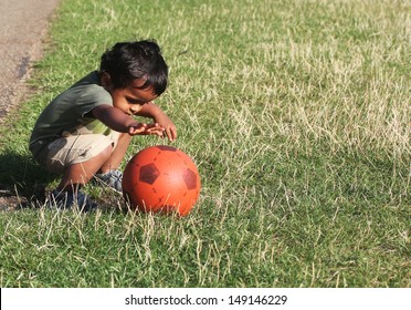 A Young Indian Toddler Playing With A Red Ball In A Green Grass Of A Garden Or A Park