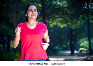 young indian woman with earphones listening music during jogging at park. - Shutterstock ID 2236272319
