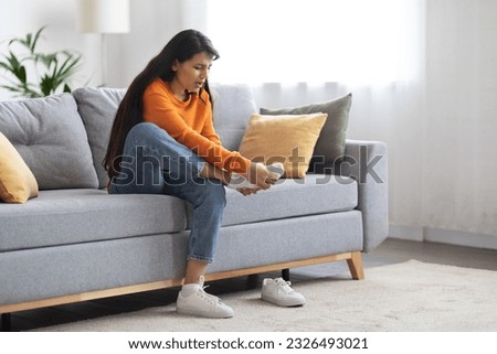 Young indian woman feeling pain in her foot at home. Healthcare and medical concept. Lady with feet intense pain sitting on a couch at home, massaging tired and aching feet, remove shoes, copy space
