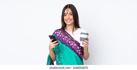 Young Indian woman isolated on white background holding coffee to take away and a mobile