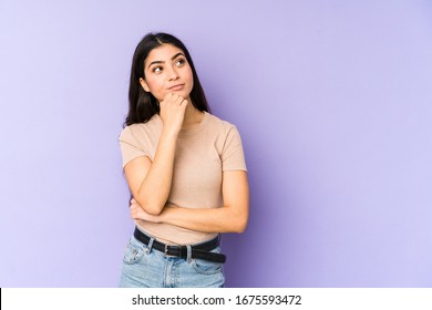 Young indian woman isolated on purple background relaxed thinking about something looking at a copy space.