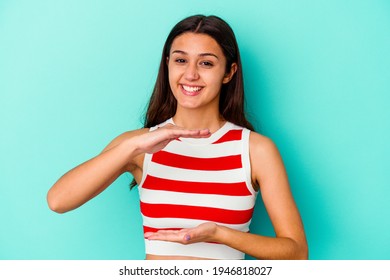 Young Indian Woman Isolated On Blue Background Holding Something With Both Hands, Product Presentation.