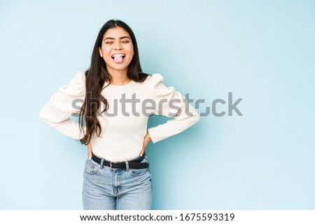 Young indian woman isolated on blue background funny and friendly sticking out tongue.