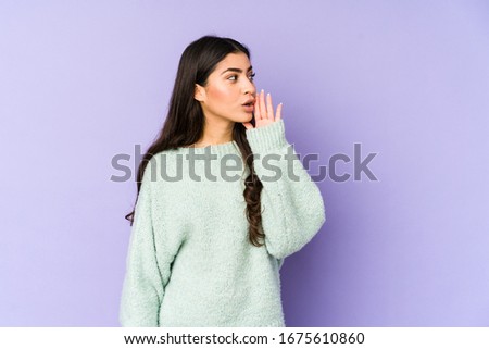 Young indian woman isolated on purple background is saying a secret hot braking news and looking aside