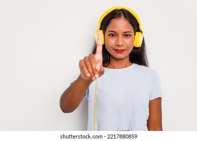 Young Indian woman listening to music wearing headphones isolated on white background showing number one with finger.