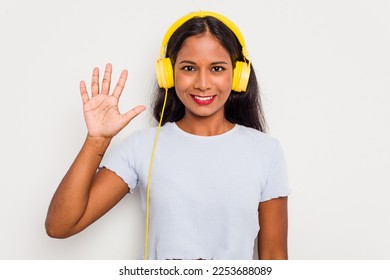 Young Indian woman listening to music wearing headphones isolated on white background smiling cheerful showing number five with fingers.