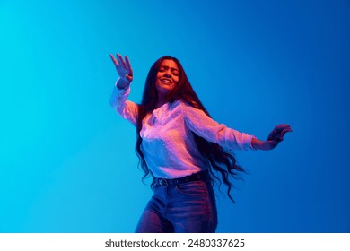 Young Indian woman with long brunette hair, waving reflecting her moves during dance in neon light against blue gradient background. Concept of music, fashion and style, rest, recreation. - Powered by Shutterstock