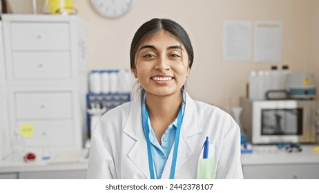 Young indian woman with long hair, smiling in a white lab coat in a medical laboratory setting, representing healthcare professionals. - Powered by Shutterstock