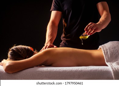 young indian woman lying on the table and getting ayurvedic massage with organic oil or honeyed in dark room.massagist male pouring out client back