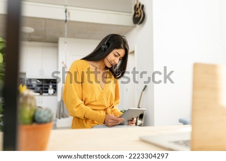 Young indian woman making a call with a tablet and headset with microphone. Millennial hindu female at home.
