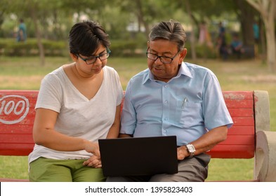 Young Indian Woman Manager In Western Formals / Shirt Helping Old Indian Man On A Laptop Promoting Digital Literacy For Elderly In A Park In New Delhi, India.Concept: Father Daughter/ Digital Literacy