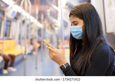 Young Indian Woman With Mask Using Phone And Sitting With Distance Inside The Train