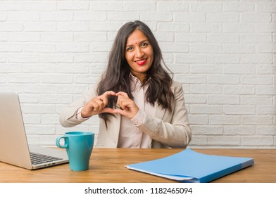 Young indian woman at the office making a heart with hands, expressing the concept of love and friendship, happy and smiling
