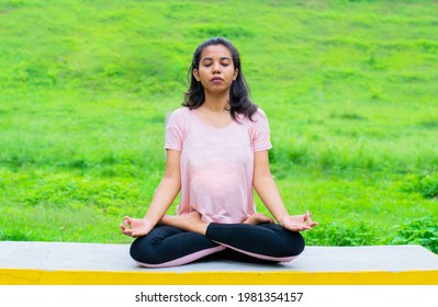Young Indian woman practicing yoga, doing Ardha Padmasana exercise, meditating in Half Lotus pose, isolated over outdoor background