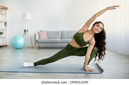 Young Indian woman practicing yoga or pilates, stretching arms and legs during domestic training, copy space. Sporty Asian lady doing flexibility exercises, enjoying healthy living at home