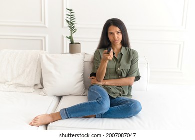 Young Indian Woman With Remote Control Watching Boring TV Series, Looking Unhappy And Tired, Mixed Race Female Watching Tv In The Living Room At Home