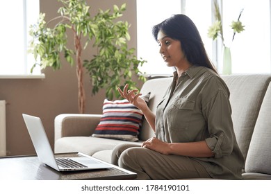 Young Indian Woman Remote Worker Or Distance Teacher Tutor Speaking To Webcam Video Conference Calling On Laptop Computer Sitting On Sofa At Home Office. Virtual Meeting Online Job Interview Call.