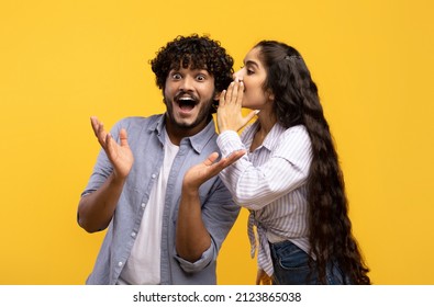 Young indian woman sharing secrets with her excited boyfriend, millennial couple whispering gossips to each other over yellow studio background - Shutterstock ID 2123865038