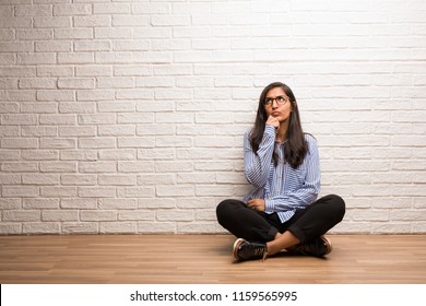 Young Indian Woman Sit Against A Brick Wall Doubting And Confused, Thinking Of An Idea Or Worried About Something