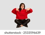 Young indian woman sitting on the floor cut out isolated points down with fingers, positive feeling.