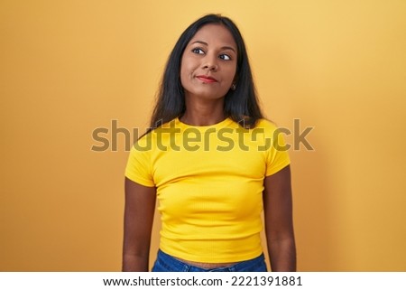 Young indian woman standing over yellow background smiling looking to the side and staring away thinking. 