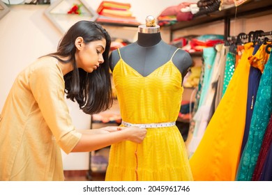 Young Indian Woman Tailor Fashion Designer Pr Dressmaker Checking Measurements And Fitting Of Dress, Tailoring Clothing On Mannequin Garment Workshop, Atelier Or Studio. Small Business Owners In Inda