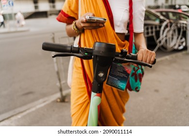 Young Indian Woman Using Cellphone While Standing With Powered Scooter Outdoors