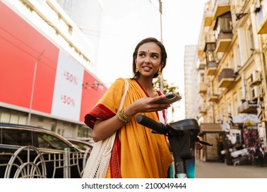 Young Indian Woman Using Cellphone While Standing With Powered Scooter Outdoors