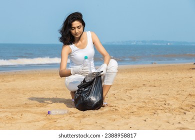 Young indian woman volunteer picking bottle into plastic black bag for cleaning beach. Environmental conservation and ecology concept. - Powered by Shutterstock