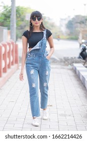 Young Indian Woman Walking On The Street Wearing Sunglasses And Blue Denim Jump Suit