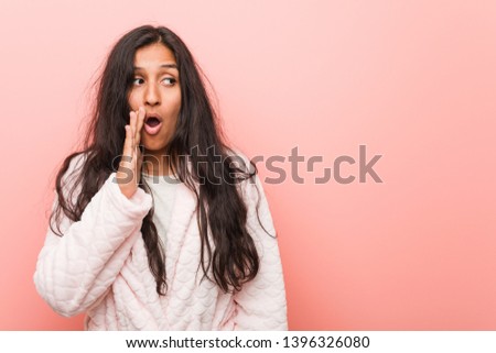 Young indian woman wearing pajama is saying a secret hot braking news and looking aside