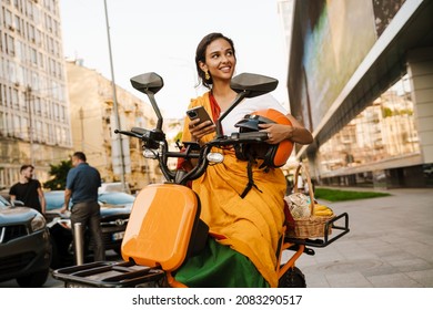 Young Indian Woman Wearing Sari Using Cellphone While Sitting On Scooter Outdoors