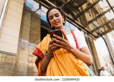 Young Indian Woman Wearing Sari Using Mobile Phone While Standing At City Street