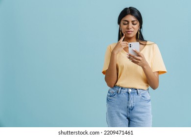 Young indian woman wearing t-shirt using mobile phone isolated over blue background